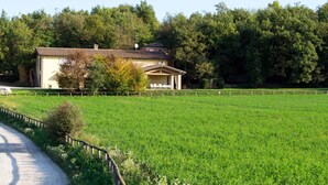 Une maison de campagne avec une allée pavée, entourée d’un champ clôturé et d’arbres denses.