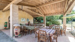 An outdoor patio with wooden tables and chairs, a brick chimney, and a decorative mushroom house.