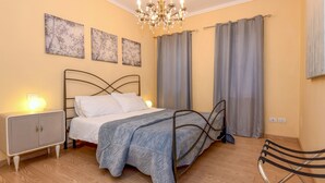 Une chambre à coucher avec un lit, une table de chevet, une lampe, des rideaux et un lustre.