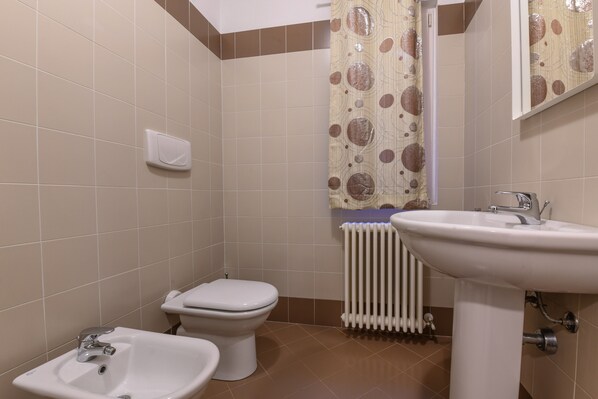A bathroom with a toilet, bidet, sink, and a radiator.