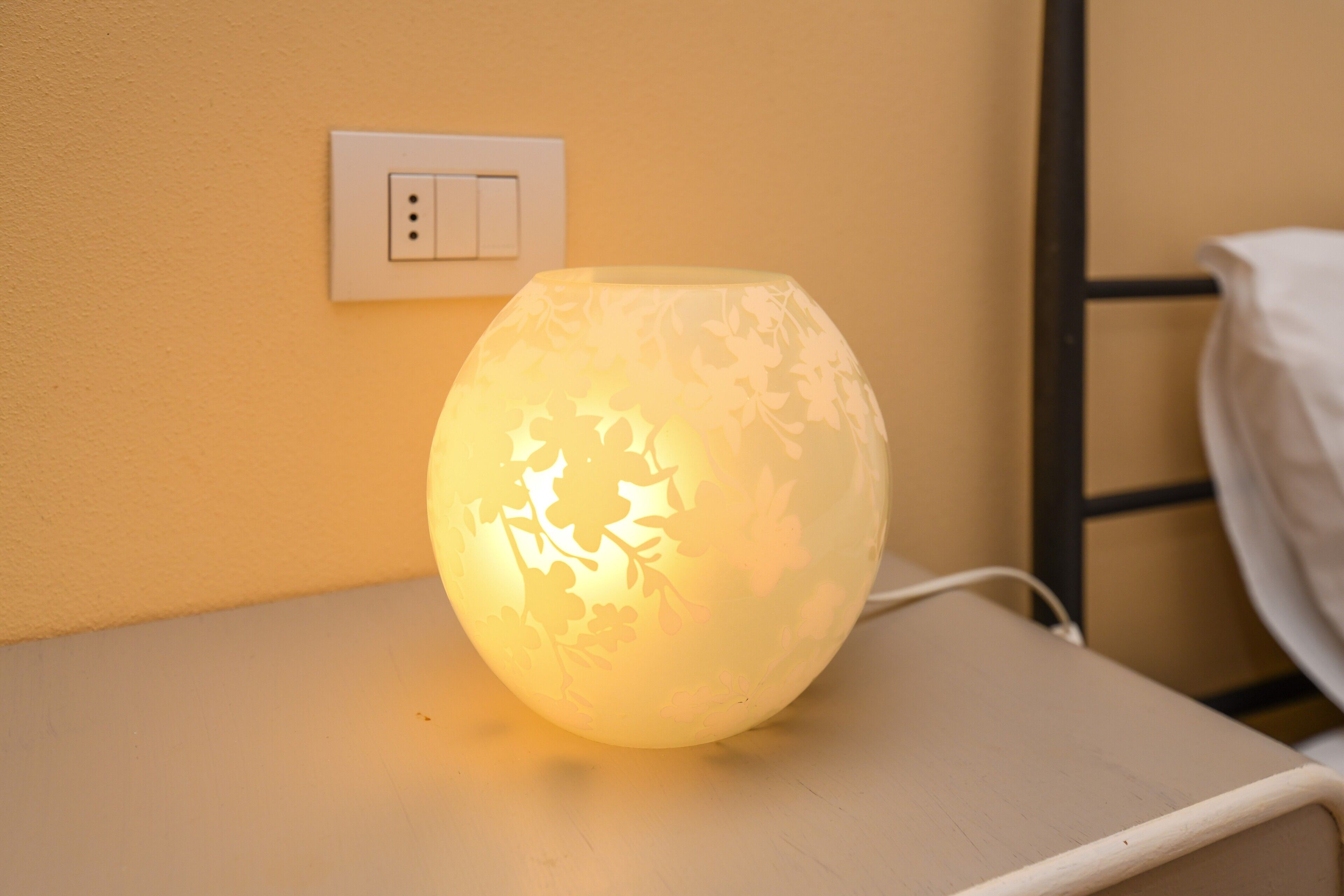 A bedside table with a lamp, a power outlet, and a bed frame.