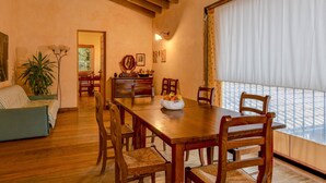 A dining area with a wooden table and chairs, a bowl of fruit, and a view through a window with curtains. - Comfortable Apartment Vittorio in Agriturismo Colleincanto (Gavardo)