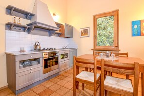 A kitchen with a stove, oven, and cabinets, a dining table with chairs, and a window with a view of trees.