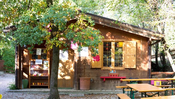 A wooden cabin with a tree in front, picnic tables, and a small shop with a 'Like' sign. - Comfortable Apartment Vittorio in Agriturismo Colleincanto (Gavardo)
