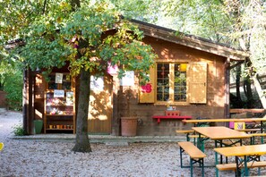 A wooden cabin with a tree in front, picnic tables, and a small shop with a 'Like' sign.