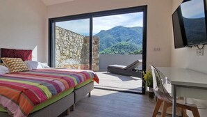 Quarto com uma cama grande, uma escrivaninha e vista para montanhas através de uma porta de vidro deslizante.