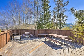 Une terrasse en bois, agrémentée de tables de pique-nique et de bancs, entourée d’arbres et d’une clôture en bois.