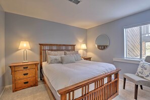 Une chambre à coucher avec un lit en bois, deux tables de chevet avec des lampes, un miroir rond et une fenêtre avec des stores.