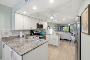 A modern kitchen with white cabinets, a granite countertop, a built-in microwave, and a ceiling fan. - 🌺Sandpebble 1E, 2 bed/2 bath & Ground-Level! Beach equipment provided! (Sanibel)