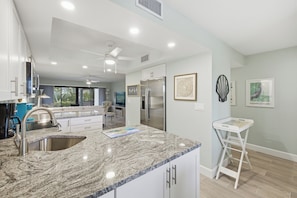 A modern kitchen with granite countertops, stainless steel appliances, and a white island. - 🌺Sandpebble 1E, 2 bed/2 bath & Ground-Level! Beach equipment provided! (Sanibel)