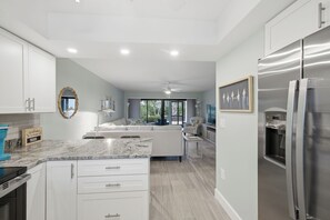 A modern kitchen with white cabinetry, a marble countertop, a stainless steel refrigerator, and a water dispenser. - 🌺Sandpebble 1E, 2 bed/2 bath & Ground-Level! Beach equipment provided! (Sanibel)