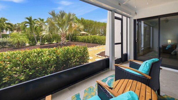 Ein Balkon mit Korbmöbeln, einem Deckenventilator und Blick auf einen angelegten Garten mit Palmen.