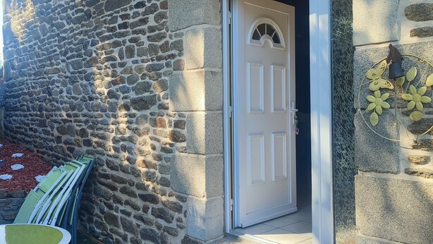 A stone building with a white door, a small outdoor seating area, and a decorative butterfly wall piece. - Vacation home Côtes d'Armor in the commune of Quessoy (Quessoy)