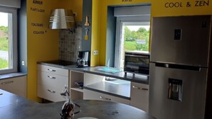 A modern kitchen with a stainless steel refrigerator, a coffee maker, and a window with a view of greenery. - Vacation home Côtes d'Armor in the commune of Quessoy (Quessoy)