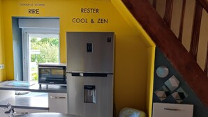 A kitchen with a refrigerator, a sink, and a trash bin. There is a table with a bag of groceries and a decorative item. The walls are painted yellow and blue. - Vacation home Côtes d'Armor in the commune of Quessoy (Quessoy)