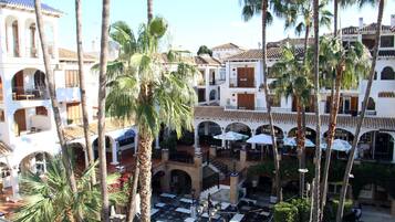 A courtyard with outdoor seating, palm trees, and buildings with tiled roofs.