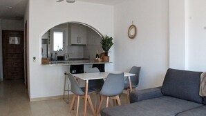 Ein modernes Wohnzimmer mit grauem Sofa, einem Esstisch mit Stühlen und einer Küchenzeile mit Schränken und einer Pflanze.