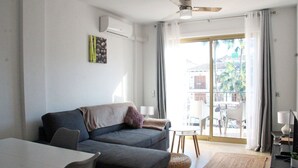 Ein modernes Wohnzimmer mit einer Couch, einem Esstisch und einem Balkon mit Gartenmöbeln.