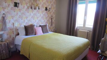 A hotel room with a bed, a nightstand, a window with curtains, and a wall with a leaf pattern.