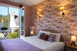 A bedroom with a bed, a balcony with a table and chairs, and a wall with a tree pattern.