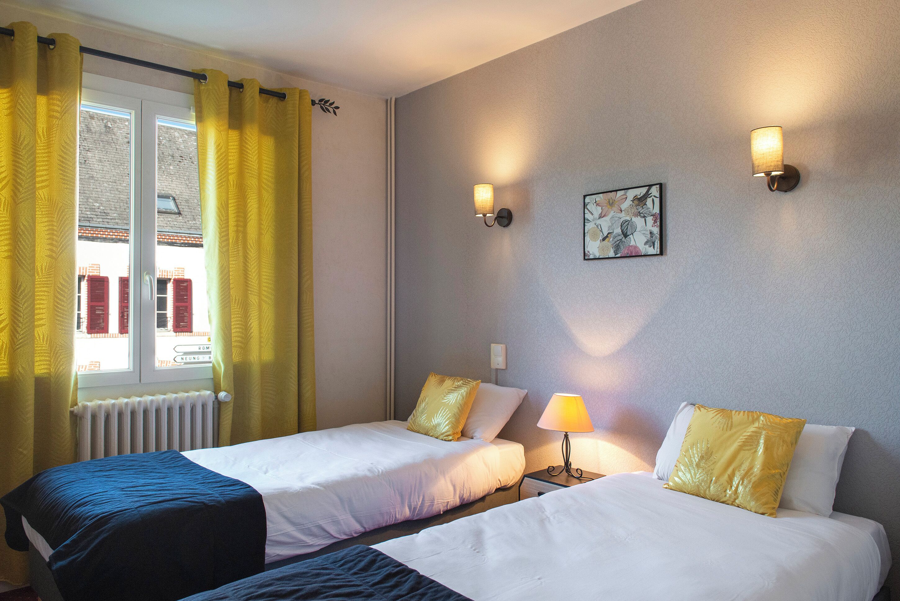 Een hotelkamer met twee bedden, een raam met gele gordijnen, een radiator en twee wandlampen.
