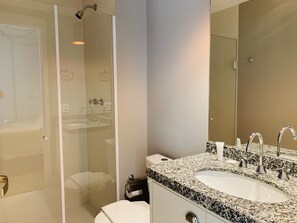A modern bathroom with a glass-enclosed shower, a white toilet, a granite countertop sink with two faucets, and a large mirror. - Akile Smart Santa Cecilia (São Paulo)