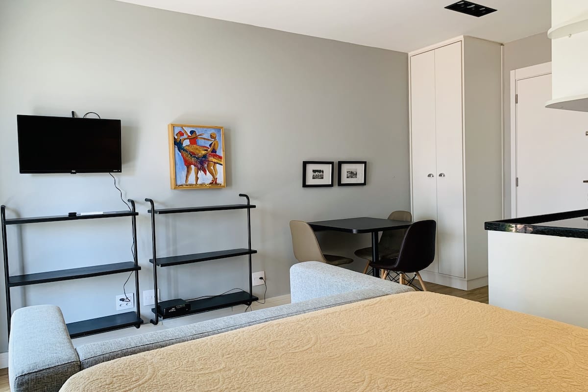 A hotel room with a bed, a desk, a chair, a TV, and artwork on the wall.