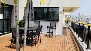Een terras op het dak met een tafel, stoelen, een palmboom en uitzicht over de stad.