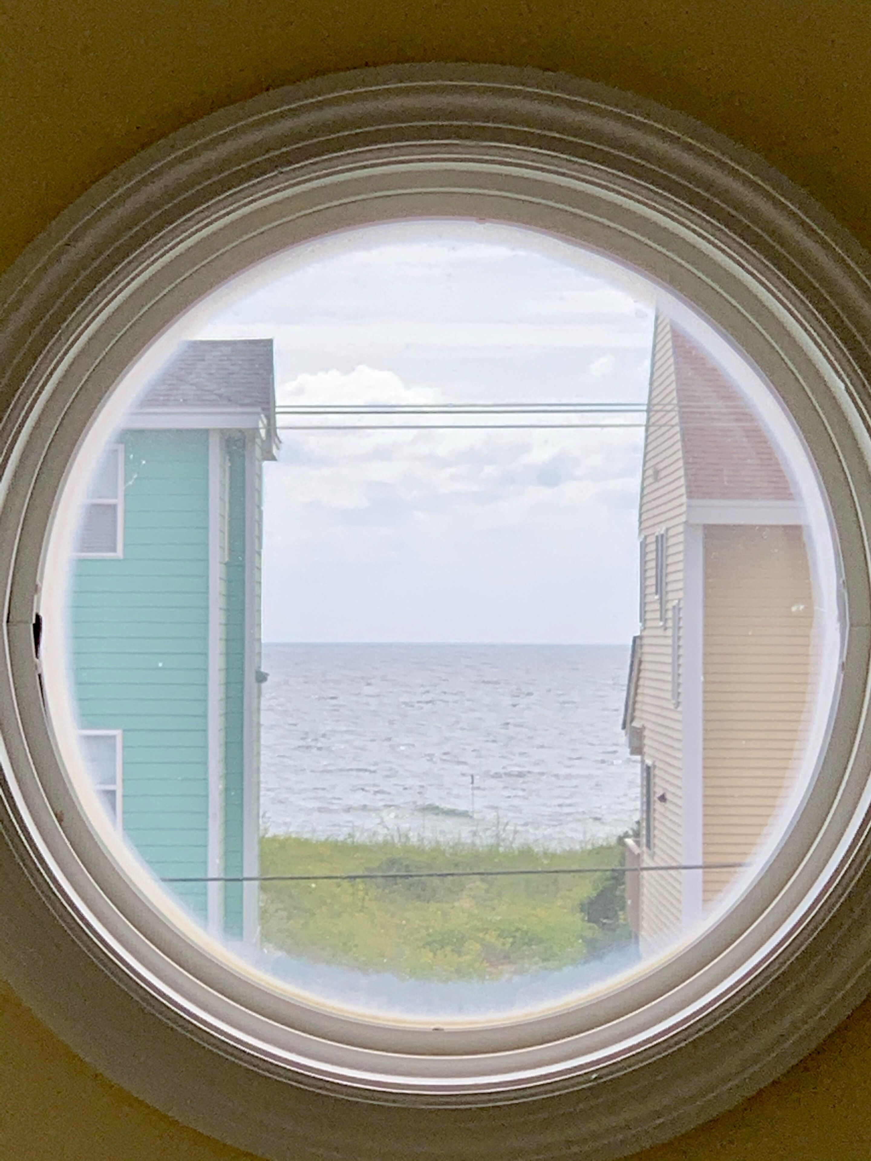A circular window with a view of the sea and two houses.