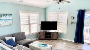 A living room with a sofa, a coffee table, a TV on a wooden stand, and a ceiling fan. - Just steps to the beach! 🏝 Surf City Beach House (Surf City)