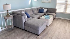 A living room with a grey sectional sofa, a round table with a lamp, and a wicker coffee table. - Just steps to the beach! 🏝 Surf City Beach House (Surf City)
