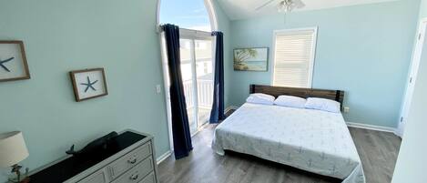 A bedroom with a bed, dresser, ceiling fan, and a view through a door.