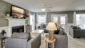 A living room with a fireplace, grey sofas, a TV, and a ceiling fan.