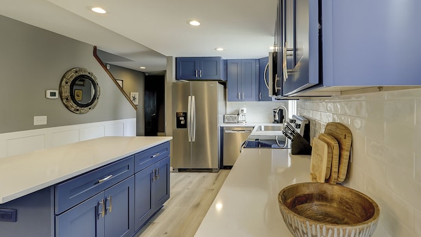 A modern kitchen with blue cabinets, stainless steel appliances, and a wooden bowl on the counter.