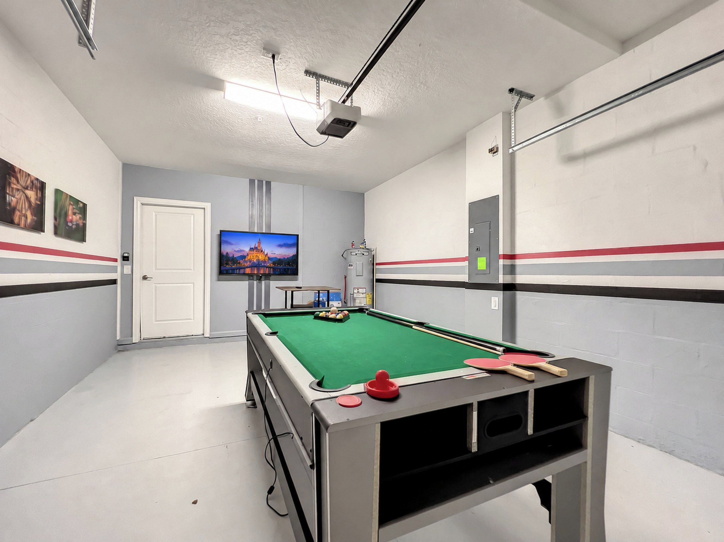 A pool table with billiard balls, a television mounted on the wall, and a door.