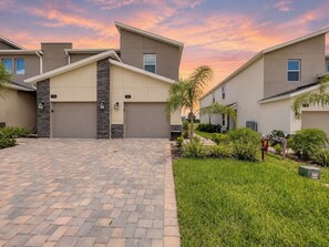 A modern residential building with a paved driveway, numbered garage doors, and well-maintained landscaping.