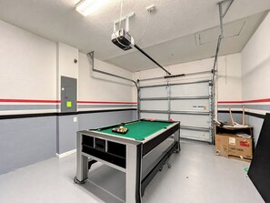 A pool table with balls, a projector, and a garage door in a room with white walls and red stripes.