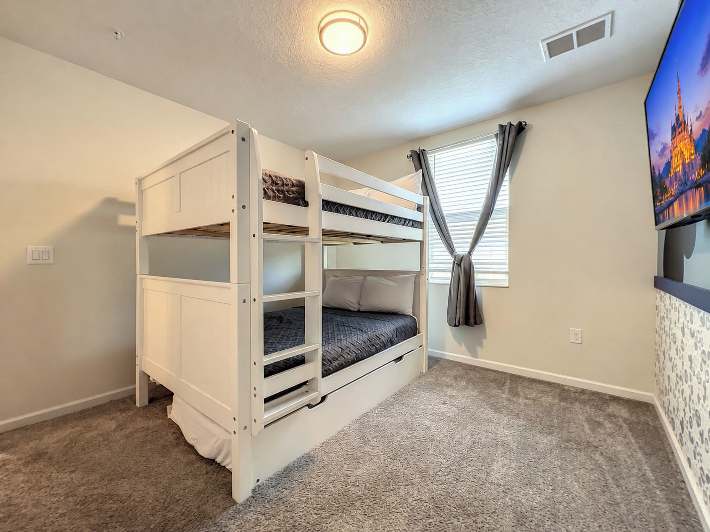A bunk bed room with a carpeted floor, a window with curtains, and a wall-mounted TV.