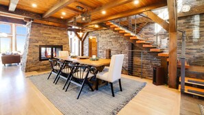 A spacious dining area with a wooden table and chairs, a fireplace, and a stone wall.