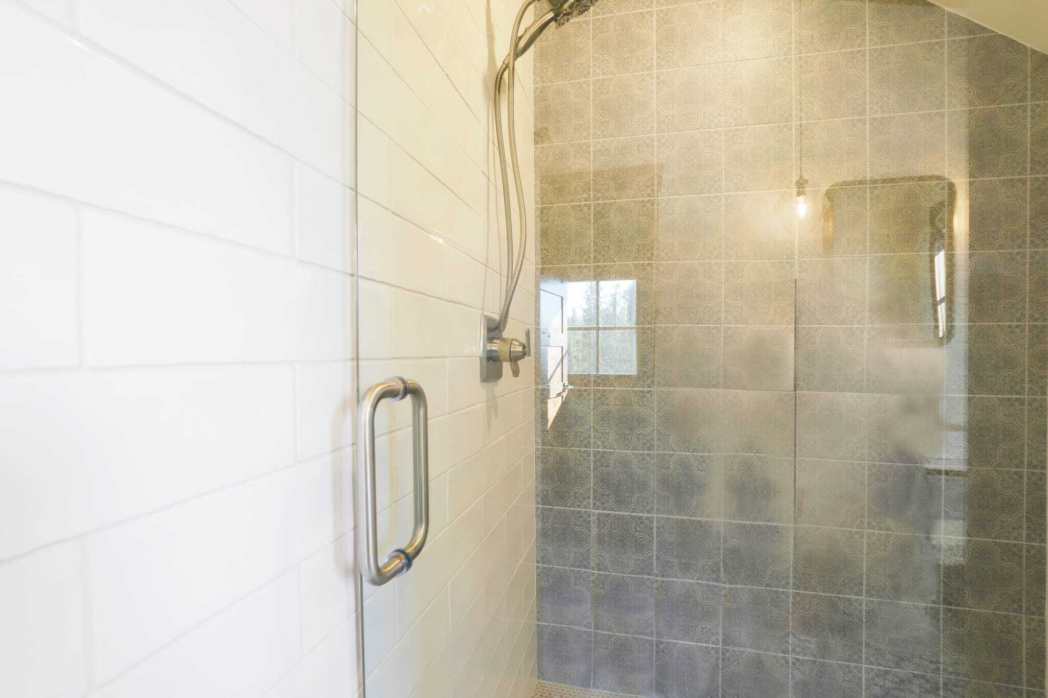 Un espace douche doté d’une porte en verre, d’une barre d’appui et d’un mur recouvert de carreaux décoratifs.