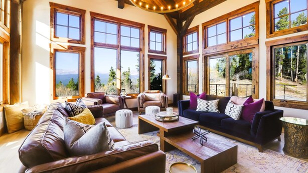 A spacious living room with large windows, leather sofas, and a wooden ceiling.
