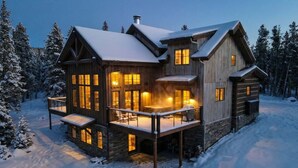 A large, multi-story wooden cabin with a balcony, surrounded by snow-covered trees.