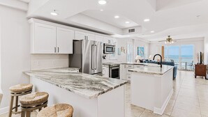 Une cuisine moderne avec des meubles blancs, un îlot central doté de tabourets, un réfrigérateur et un four à micro-ondes.