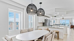 Une cuisine spacieuse dotée d’un grand îlot central, de meubles blancs et de luminaires suspendus.