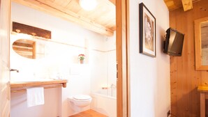 Een badkamer met een houten plafond, een wit toilet, een wastafel met spiegel en een douche.