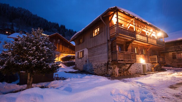 Een houten chalet met balkon, omringd door een besneeuwde omgeving en bomen.