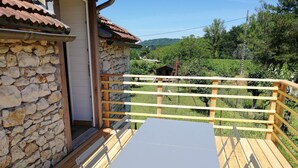A wooden deck with a table and chairs, a stone wall, and a view of a vineyard.