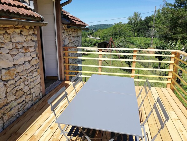 A wooden deck with a table and chairs, a stone wall, and a view of a vineyard.