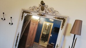 A mirror with ornate frame, wooden wardrobe, and a bathroom with a sink and mirror.