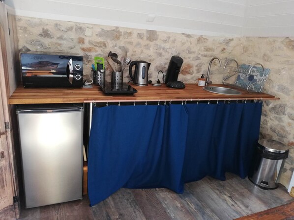 Una cocina compacta con horno integrado, cafetera, hervidor y pileta.